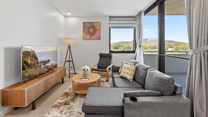 Una sala de estar moderna con un televisor de pantalla plana grande, un sofá, una mesa de centro y vistas al exterior.