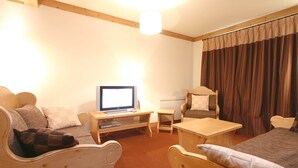 Une pièce meublée en bois, comprenant une télévision, une petite table, une chaise et un canapé.