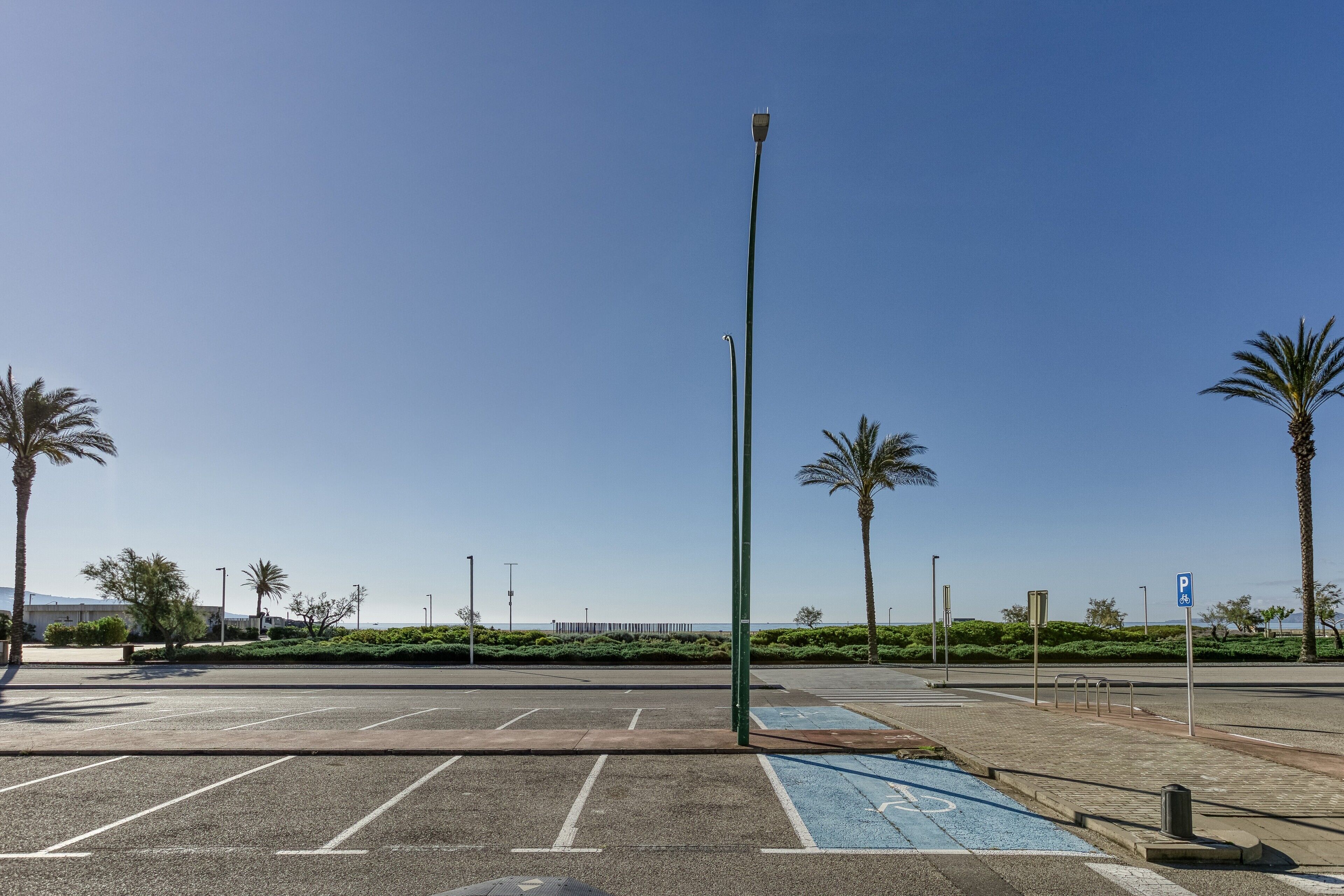 Un estacionamiento con espacios delimitados, un carril bici azul y cielo despejado.
