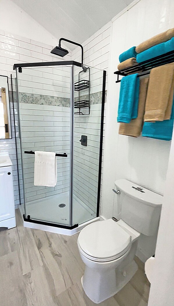A bathroom with a glass shower enclosure, a toilet, and a towel rack with towels.