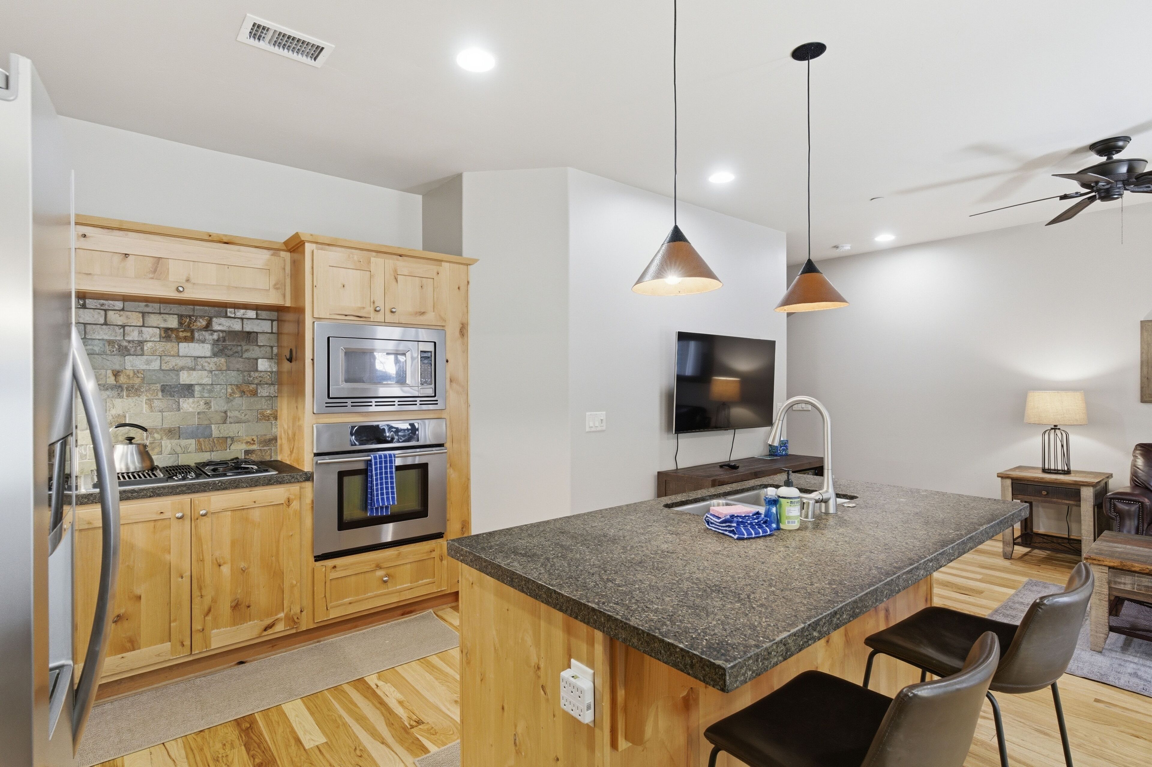 A modern kitchen with wooden cabinets, granite countertops, a built-in oven, and a central island with seating.