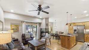 Een ruime woonkamer met een open haard, een eettafel en een keuken met houten kastjes en een roestvrijstalen koelkast.