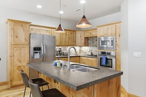 Eine moderne Küche mit Holzausstattung, Edelstahlgeräten, Granit Arbeitsplatten und Pendelleuchten.