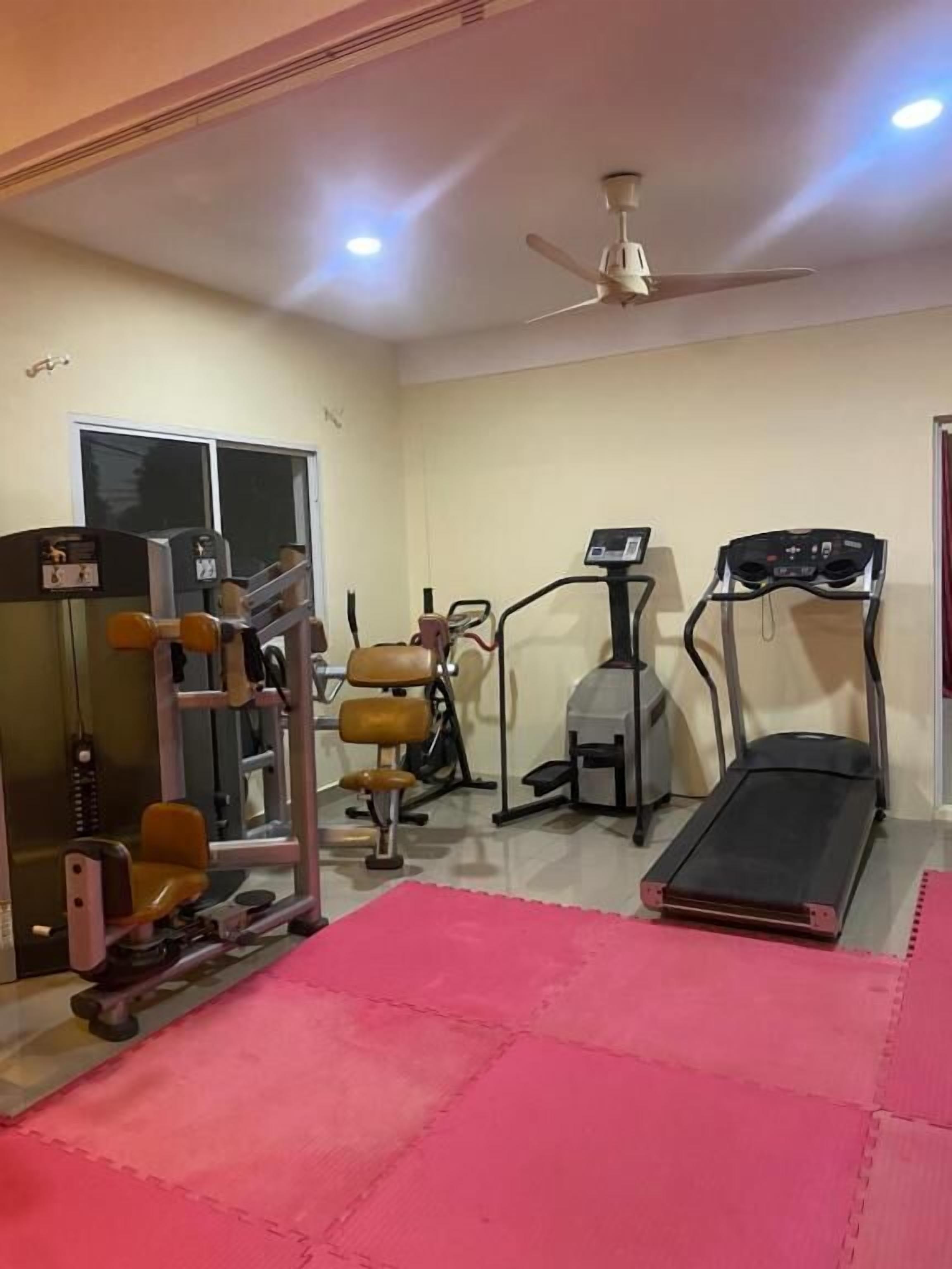 Un gimnasio con equipo de ejercicio, una cinta de correr y un ventilador de techo.