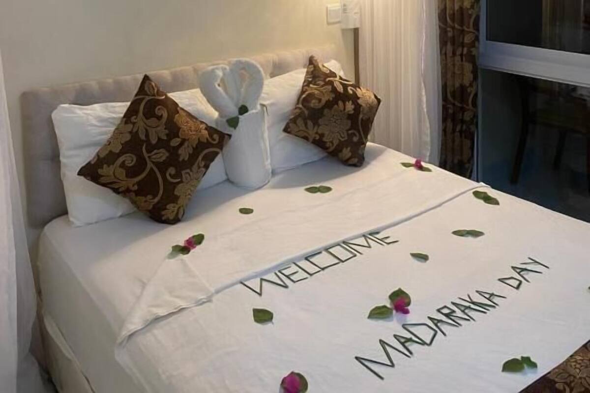 Una habitación de hotel con una cama, un cuadro enmarcado en la pared, una lámpara de noche y una ventana con cortinas.