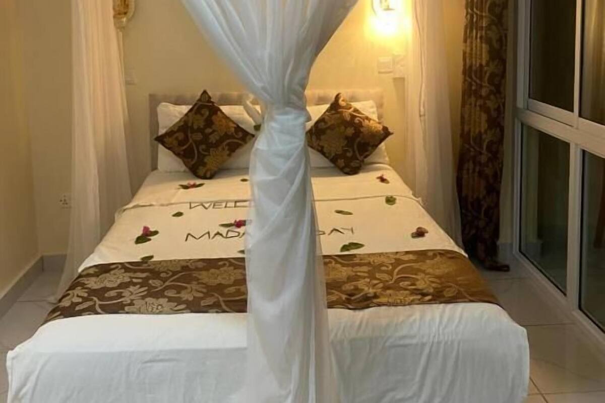 Un dormitorio con cama con dosel, lámpara de noche y ventana con cortinas.