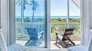 Un balcone con vista sull'oceano, una sedia di legno e una ringhiera bianca.