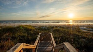 Una passerella in legno che conduce a una spiaggia con un tramonto sullo sfondo.