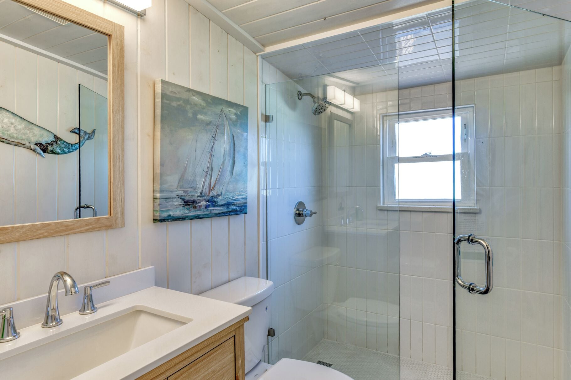 Un bagno con doccia vetrata, un lavandino con specchio e un quadro raffigurante una barca a vela.