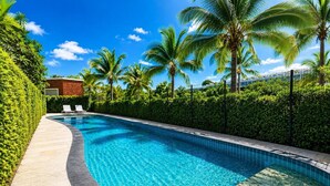 Una piscina a forma di curva, circondata da palme e un siepe.