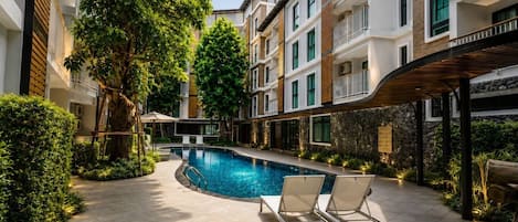 Un hotel moderno con piscina, sillas de descanso y un patio cubierto.