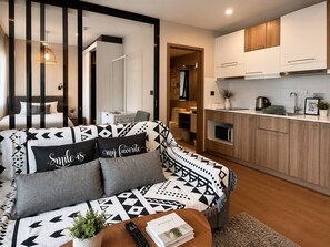 A modern living room with a sofa, a coffee table, and a kitchen area with wooden cabinets and a countertop. - Modern 1br Apartment in Rawai | 2min to beach (Rawai)