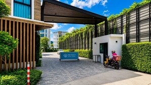 A modern building entrance with a sign, a paved pathway, and a motorbike with a delivery box. - Cozy 1br in Rawai Quiet Area balcony&fast wi-fi (Rawai)