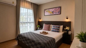 A hotel room with a bed, a nightstand, a wall-mounted air conditioner, and a window with curtains. - Cozy 1br in Rawai Quiet Area balcony&fast wi-fi (Rawai)