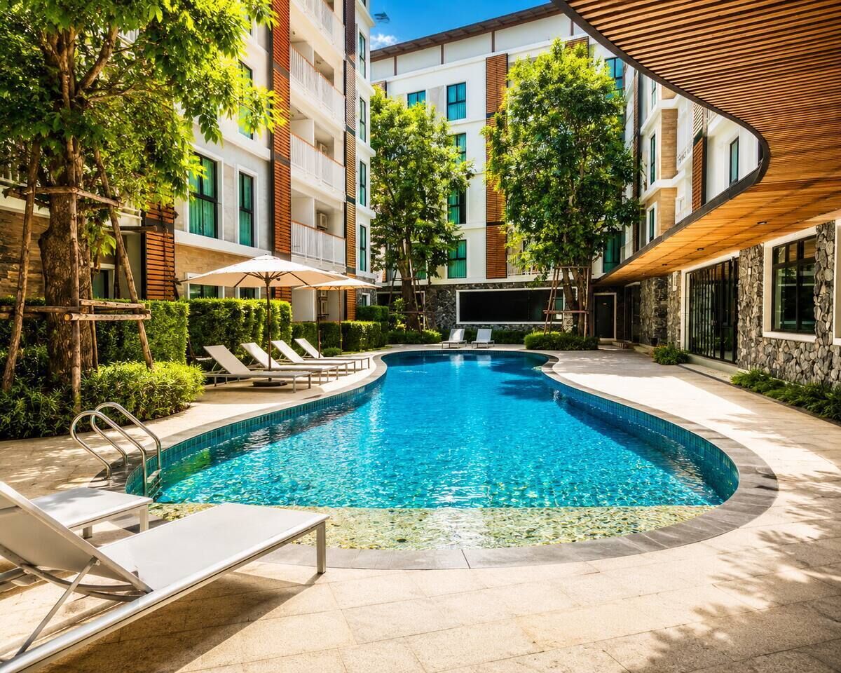 A swimming pool with lounge chairs and a covered area, surrounded by multi-story buildings with balconies.