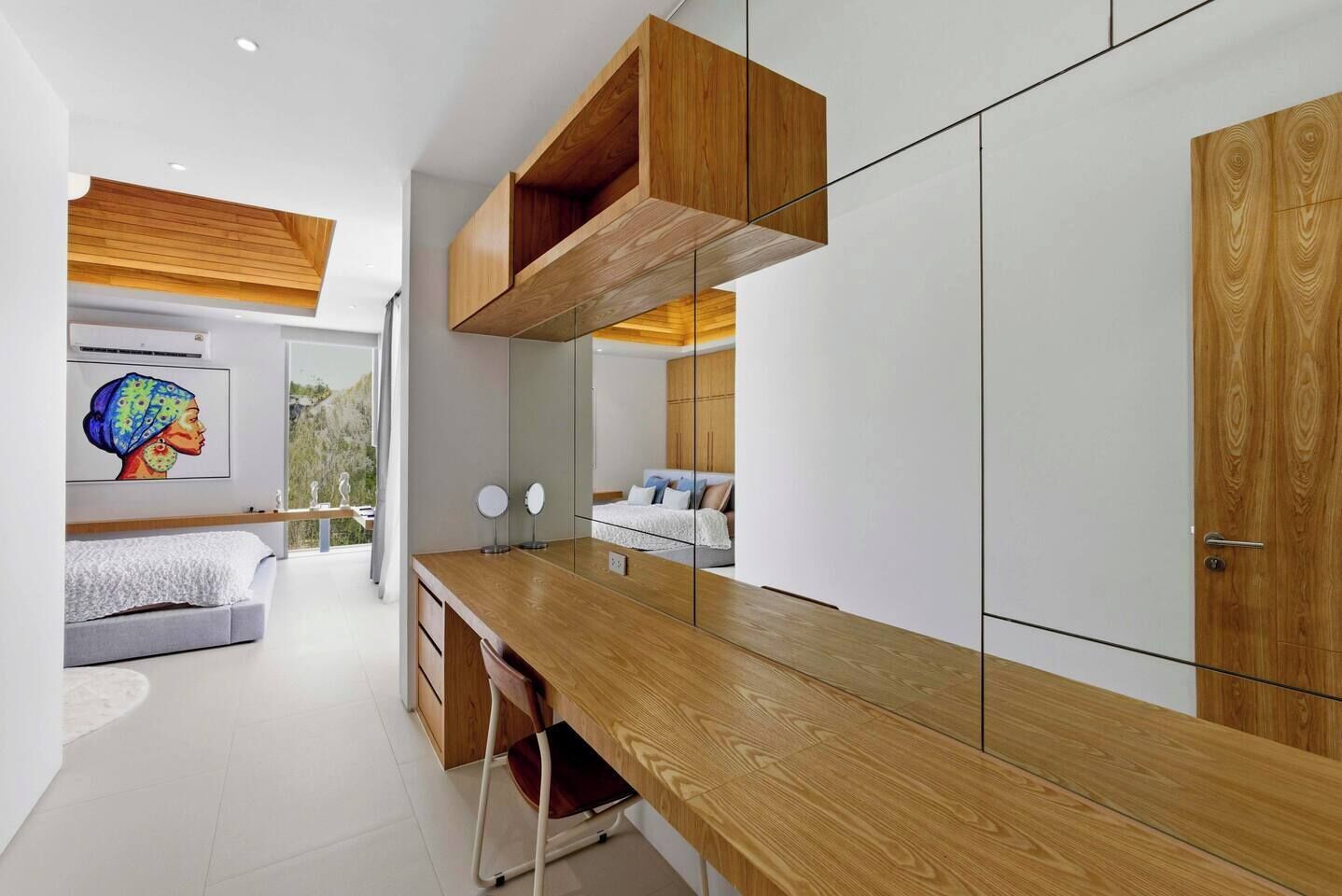 A modern bedroom with a wooden desk, a bed with a view, and a large mirror.