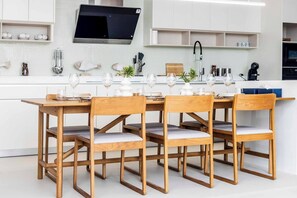 A modern kitchen with a dining area, featuring wooden furniture, a flat-screen TV, and a white tiled backsplash. - New Luxurious Villa 3 Br with private pool bangtao (Tambon Si Sunthon)