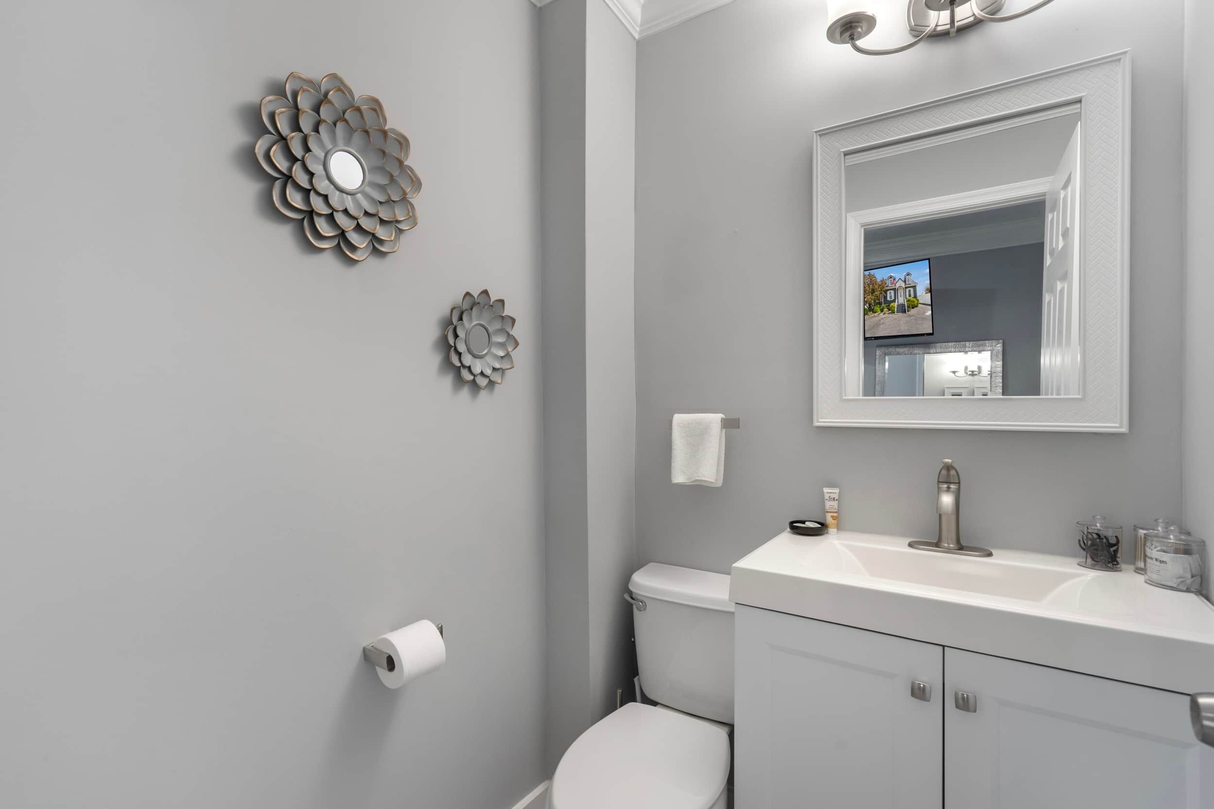 A bathroom with a toilet, sink, mirror, and decorative wall art.