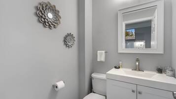 A bathroom with a toilet, sink, mirror, and decorative wall art.