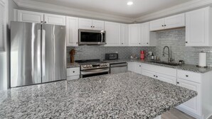 A modern kitchen with white cabinetry, granite countertops, stainless steel appliances, and a tiled backsplash. - Petite Retreat at Harper's Ferry (Bolivar)