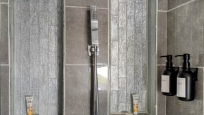 A shower area with a handheld showerhead, two bottles of shampoo, and two bottles of conditioner on a wall-mounted shelf. - Petite Retreat at Harper's Ferry (Bolivar)