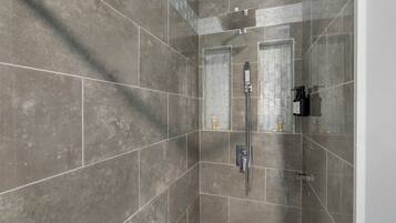 A shower with a handheld showerhead, a wall-mounted faucet, and a glass-enclosed shower area.