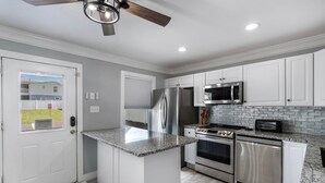 A kitchen with white cabinets, stainless steel appliances, a granite countertop, and a ceiling fan. - Petite Retreat at Harper's Ferry (Bolivar)