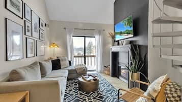 A living room with a sofa, a coffee table, a fireplace, a television, and framed pictures on the wall.