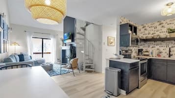 A modern kitchen with a central island, a dining area with a white table, and a living room with a sofa and a TV.