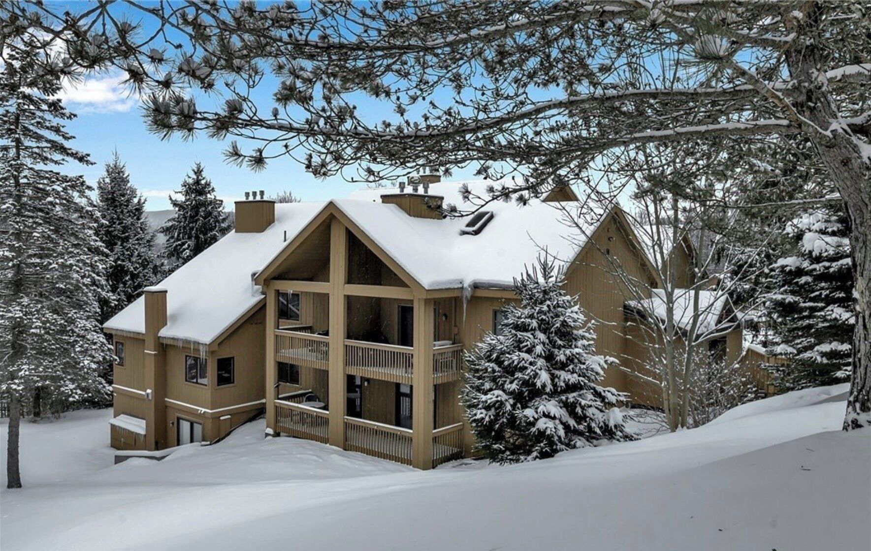 A multi-story lodge with a balcony, surrounded by snow-covered trees.