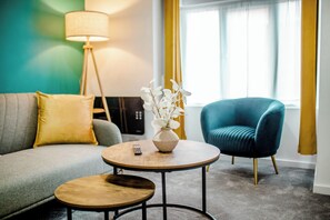 Ein modernes Wohnzimmer mit einer Couch, zwei runden Tischen, einem blauen Sessel, einer Vase mit weißen Blumen und einer Lampe.