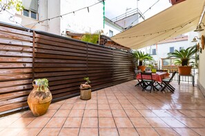 Eine Terrasse mit Holzlattenzaun, Terrakottatöpfen, einem Tisch mit Stühlen und Topfpflanzen.