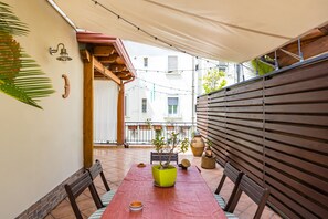 Eine Terrasse mit einem Holztisch, Stühlen, einem Blumentopf und einer Wandleuchte.