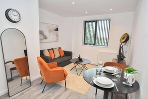 A modern living room with a sofa, two orange chairs, a coffee table, and a dining table set for two. - Bright & Spacious 1 Bedroom Apartment in Leeds (Leeds)