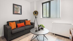 A modern living room with a grey sofa, orange cushions, a round coffee table, a floor lamp, a framed plant, and a radiator. - Bright & Spacious 1 Bedroom Apartment in Leeds (Leeds)