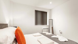 A hotel room with a bed, a chair, a window with blinds, a mirror, and a radiator. - Bright & Spacious 1 Bedroom Apartment in Leeds (Leeds)