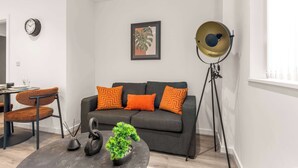 A modern living room with a grey sofa, orange cushions, a round coffee table with a plant, a floor lamp, and a framed picture on the wall. - Bright & Spacious 1 Bedroom Apartment in Leeds (Leeds)