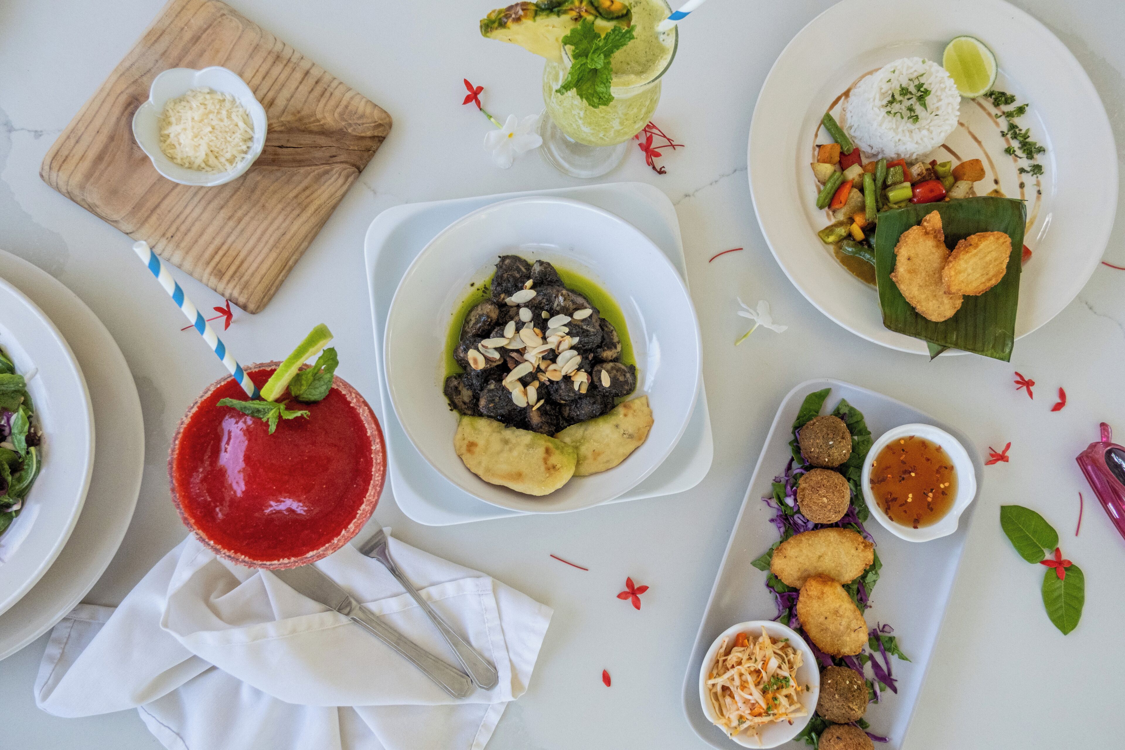 A variety of dishes on a table, including a red drink, a bowl of food with a green sauce, and a plate with rice and vegetables.