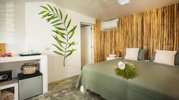 A bedroom with a bed, a small desk, a refrigerator, a wall-mounted air conditioner, and a large window.