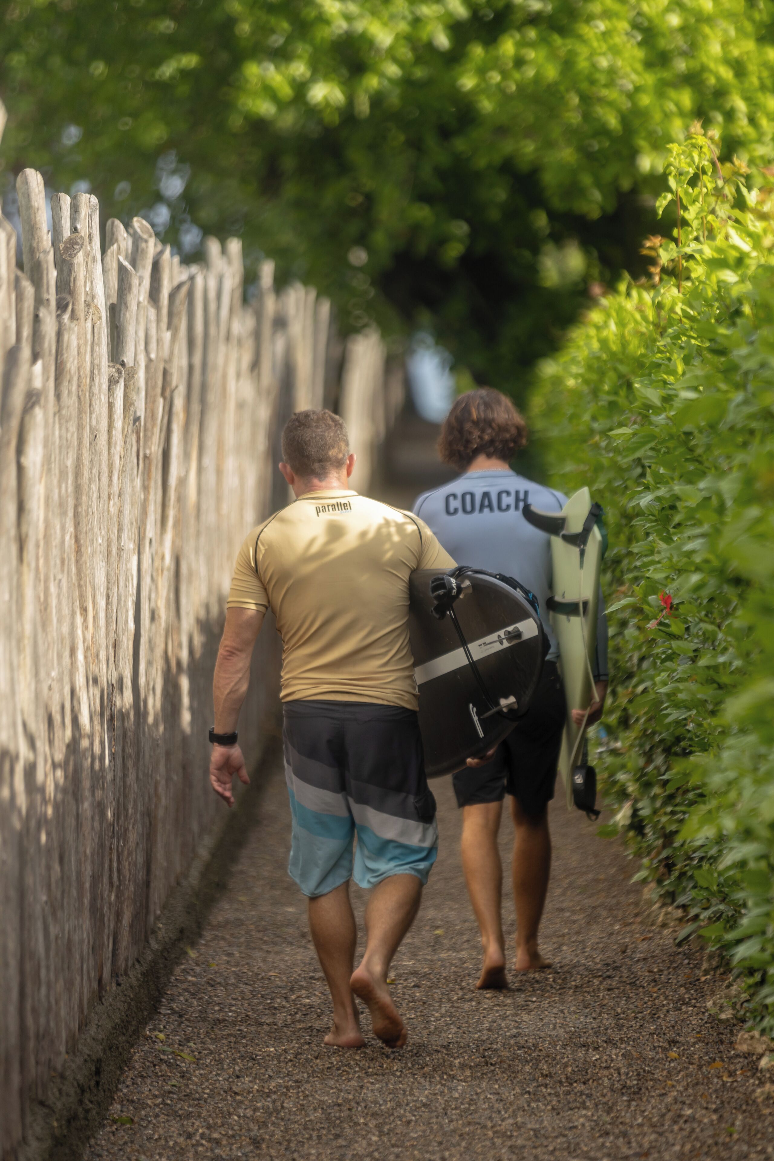 Twee personen lopen over een pad met aan één kant een houten hek en aan de andere kant groen.