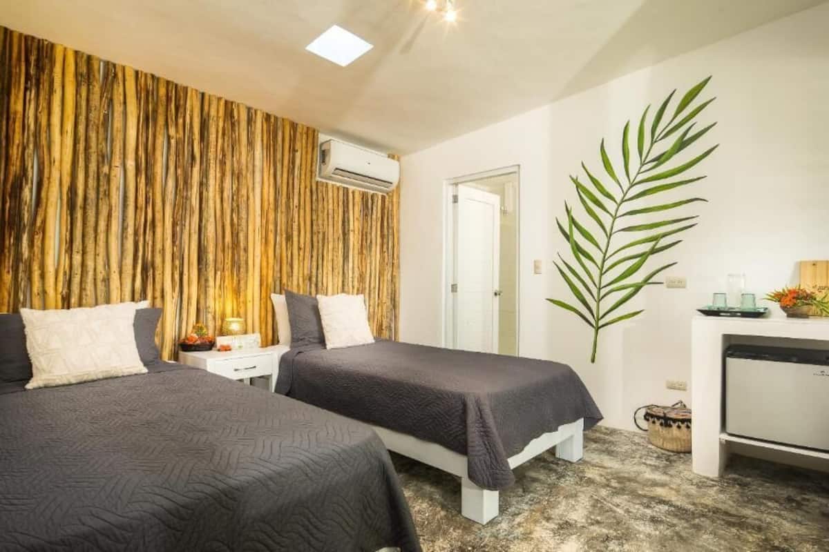 A bedroom with two beds, a wooden wall, an air conditioning unit, a desk with a plant, and a mirror.