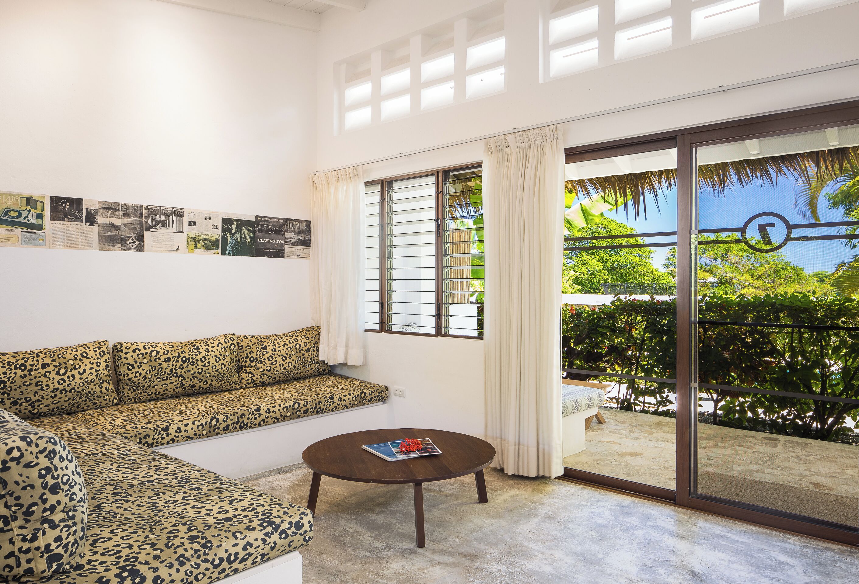 A living room with a sofa, a coffee table, a sliding glass door to a balcony, and a wall with framed pictures.