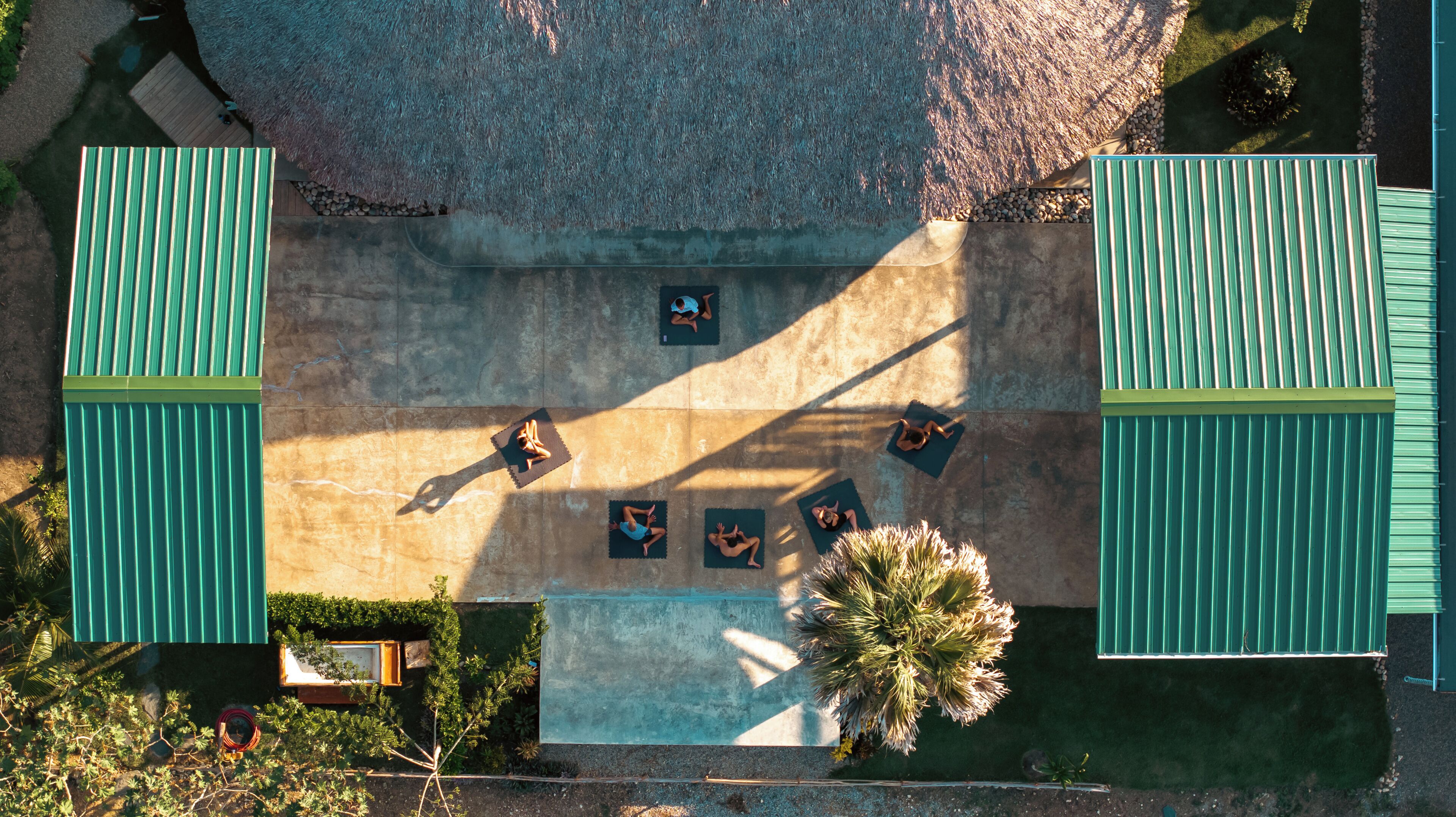 An aerial view of a rooftop with a thatched roof, green railings, and a central area with yoga mats.