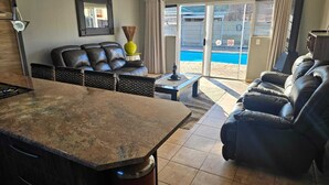 Ein modernes Wohnzimmer mit einer Steinarbeitsplatte, Ledersofas, einem kleinen Tisch und Blick auf einen Swimmingpool durch Glastüren.