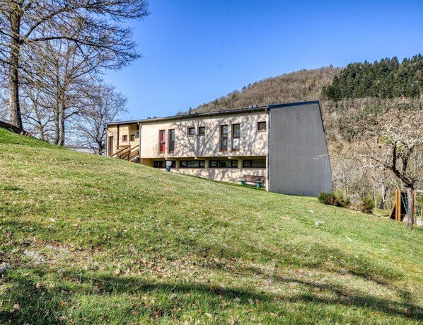A modern building with a flat roof, a sloped side, and a grassy hill in the foreground.
