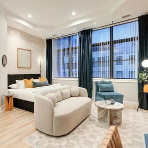 A modern hotel room with a large bed, a sofa, a small table, and a view of the city through large windows. - 718 Sansom Street  (Philadelphia)