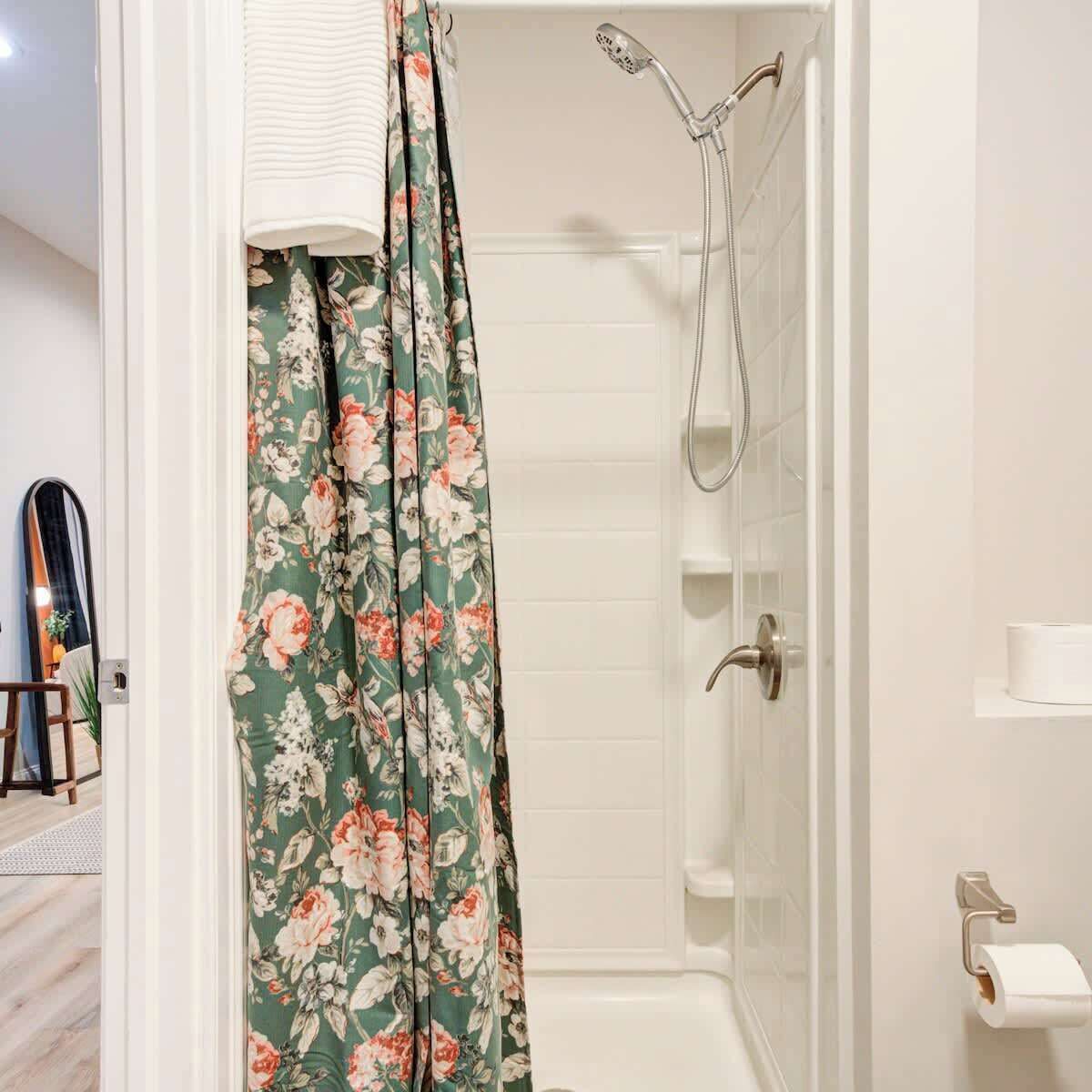 A bathroom with a shower, a toilet paper holder, and a mirror.