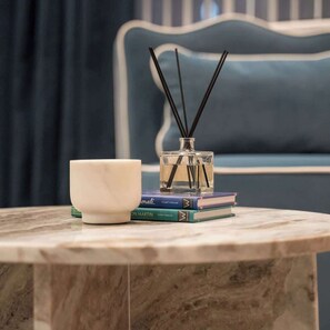 Una mesa de mármol con un bol blanco, una botella de vidrio con ramitas de caña y una pila de libros.
