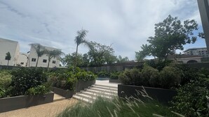 A landscaped outdoor area with steps leading to a building, surrounded by greenery and palm trees. - Bantree Apartment by Cozy (Accra)