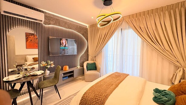 A modern hotel room with a bed, a dining table, a TV, and a seating area. - Bantree Apartment by Cozy (Accra)